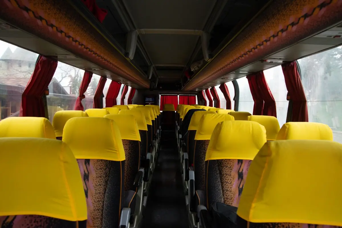 Pasillo de un autocar con filas de asientos de respaldo amarillo y cortinas rojas, sin pasajeros